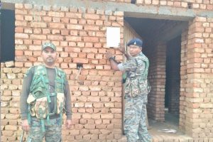 नक्सली रवींद्र गंझू के घर इश्तेहार चिपकाते पुलिसकर्मी