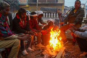 ठंड से राहत पाने के लिए आग के पास बैठे लोग